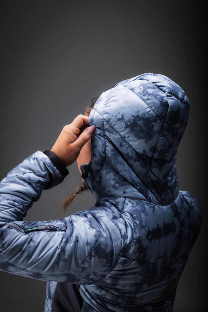 A person wearing a grey patterned puffer jacket with zipped pockets.