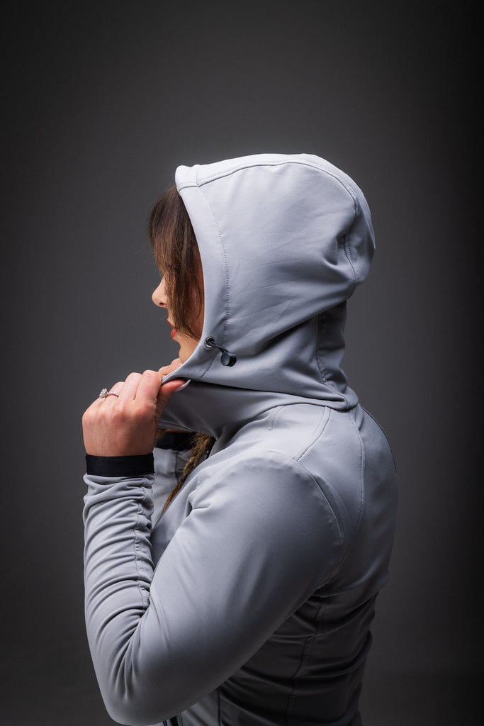 A person wearing a grey midlayer with a hood and zipped pockets, paired with blue patterned leggings.