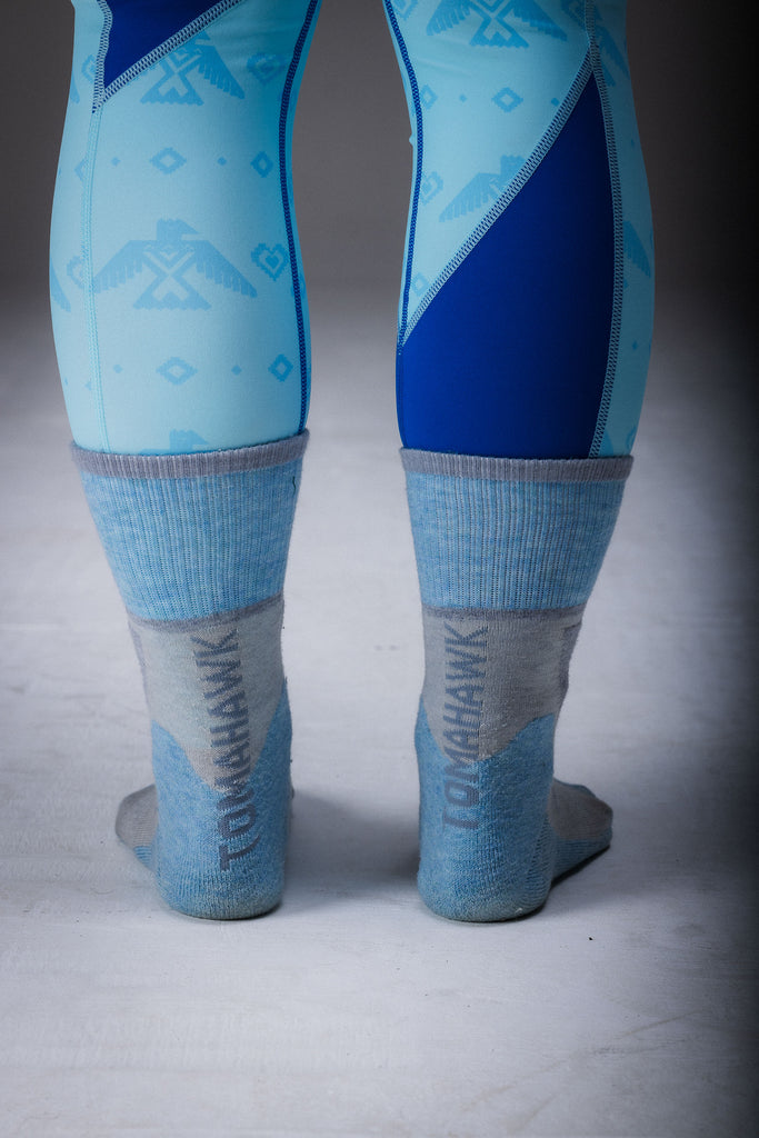 A pair of merino wool hiking socks, with the upper part in blue and the lower part in grey, standing upright on a plain background.