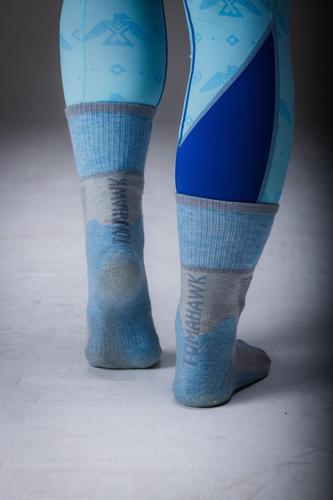 A pair of merino wool hiking socks, with the upper part in blue and the lower part in grey, standing upright on a plain background.