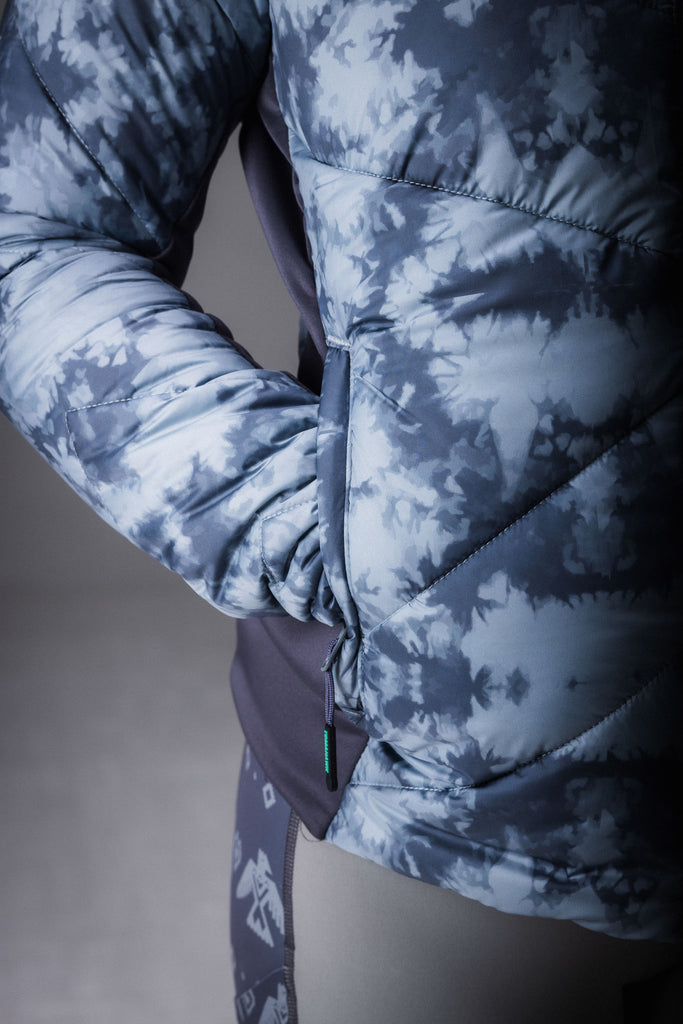 A person wearing a grey patterned puffer jacket with zipped pockets.