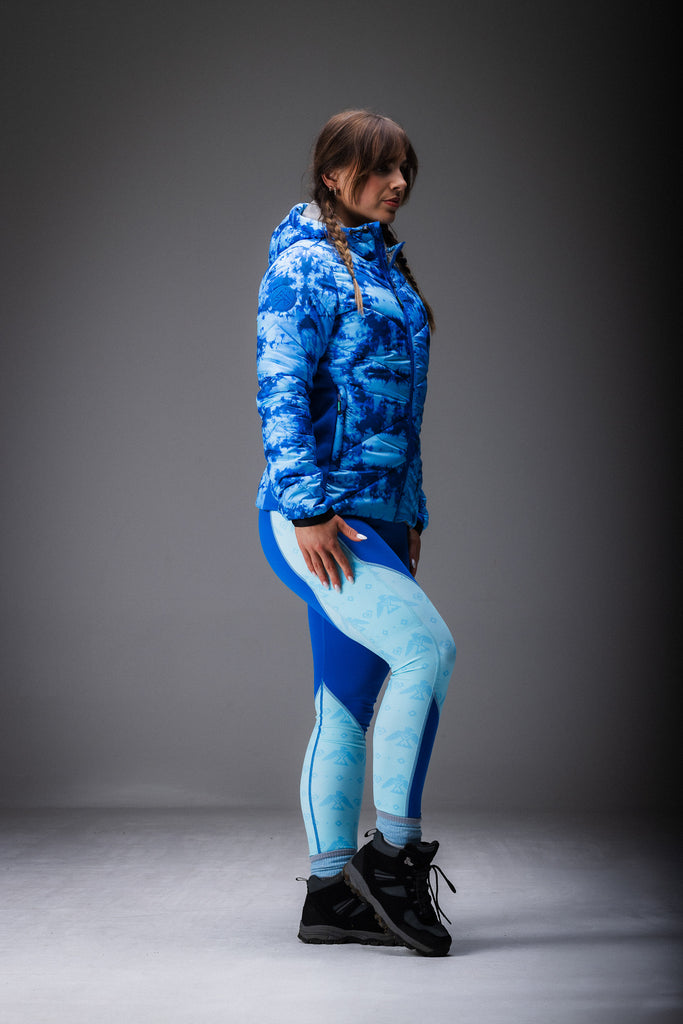 A person wearing a blue tie-dye patterned puffer jacket with zipped pockets, standing in a natural outdoor setting.