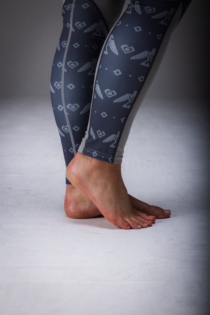 A person standing in a studio setting, wearing gray leggings with a geometric pattern, including black accents that resemble a tribal design.