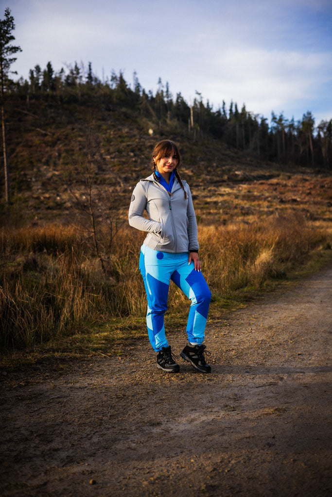 A person wearing a grey midlayer with a hood and zipped pockets, paired with blue patterned leggings.