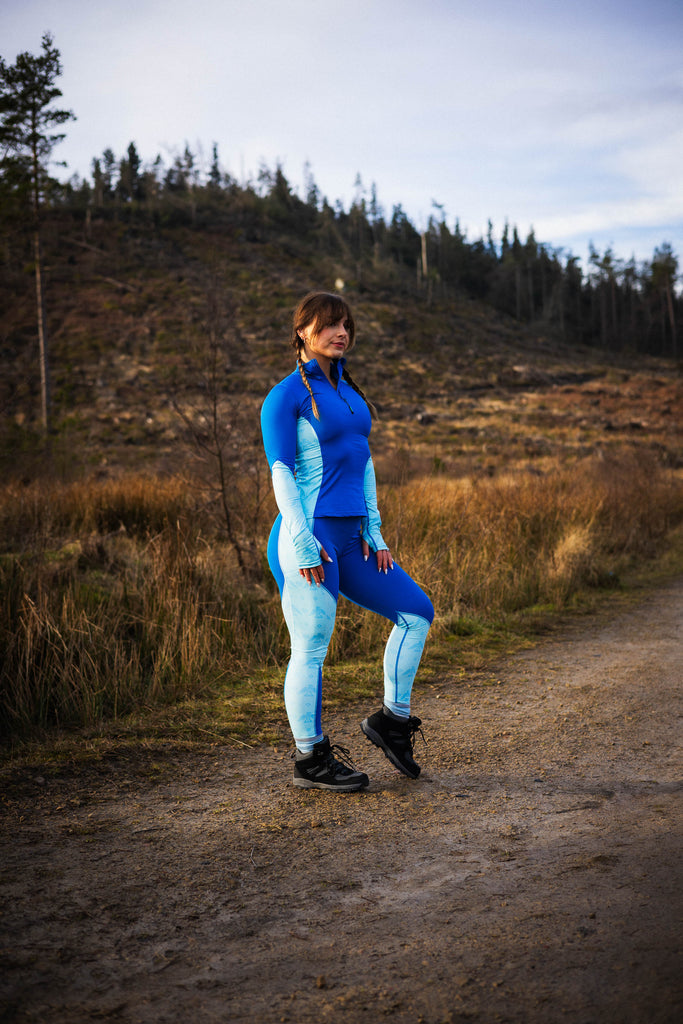 A person standing, wearing blue leggings with a geometric pattern, and a black sports bra.