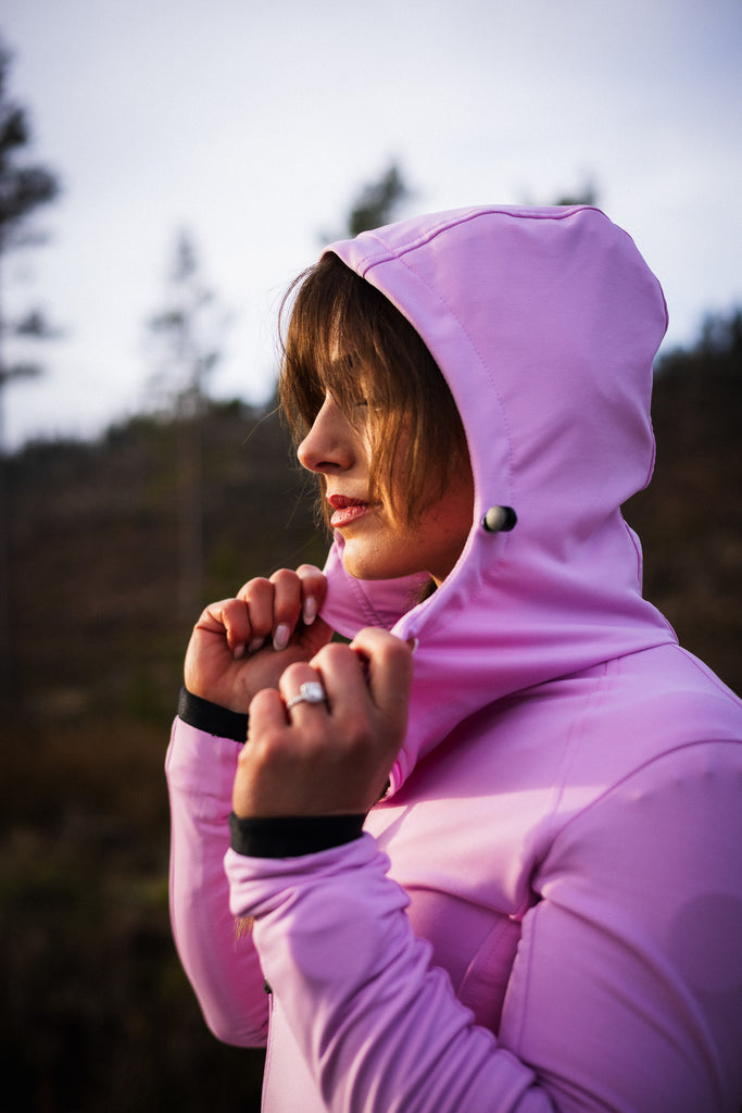 A person wearing a pink midlayer with a hood, zipped pockets, and an off-centred zip fastener, paired with patterned leggings and socks.
