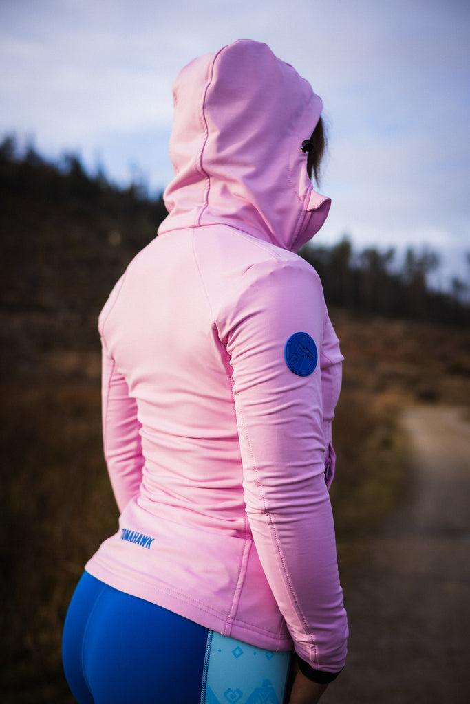 A person wearing a pink midlayer with a hood, zipped pockets, and an off-centred zip fastener, paired with patterned leggings and socks.