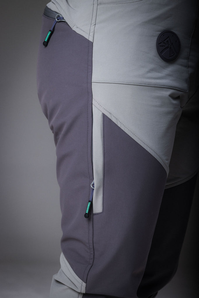 A woman standing, wearing high-waisted grey pants with reinforced waterproof panels at the knee and seat, suitable for hiking.